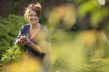 Porträt einer glücklichen, selbstbewussten Frau, die im Garten frische Kartoffeln erntet - CAIF30874