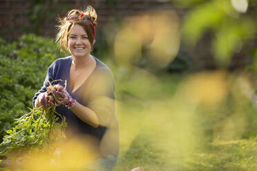 Portrait happy confident woman harvesting fresh potatoes in garden - CAIF30874