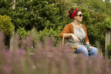 Frau mit Sonnenbrille macht eine Pause von der Gartenarbeit im Sommer Hinterhof - CAIF30894