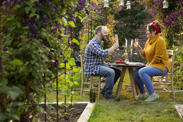 Couple enjoying champagne at table in idyllic summer garden - CAIF30902