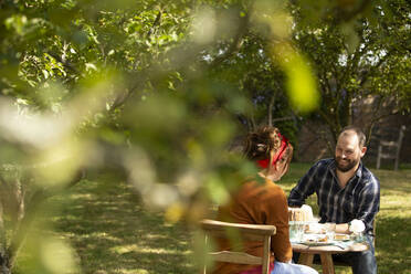 Paar genießt Kuchen an einem Tisch in einem sonnigen Sommer-Obstgarten - CAIF30909