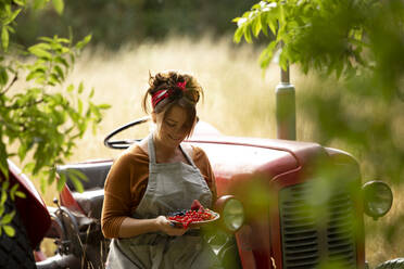 Happy woman with fresh harvested red currants at tractor - CAIF30910