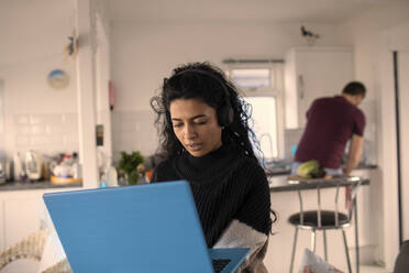 Frau mit Kopfhörern und Laptop, die von zu Hause aus arbeitet - CAIF30945