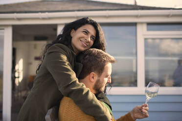 Glückliches Paar, das sich umarmt und Wein auf der Veranda trinkt - CAIF30989