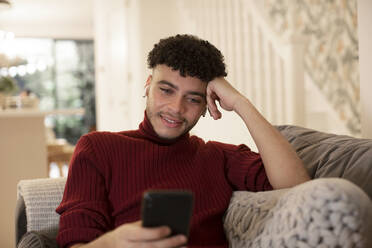 Junger Mann mit Smartphone auf dem Wohnzimmersofa - CAIF31043