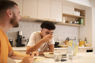 Ein schwules männliches Paar isst und benutzt einen Laptop am Küchentisch - CAIF31058