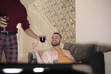 Glückliches schwules männliches Paar, das zu Hause Rotwein trinkt und fernsieht - CAIF31063
