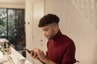 Young man using smart phone in kitchen - CAIF31080