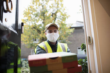 Portrait delivery man in face mask delivering pizza at front door - CAIF31104