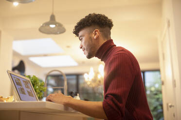 Junger Mann arbeitet von zu Hause aus am Laptop in der Küche - CAIF31105