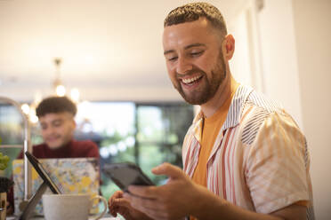 Happy young man using smart phone at home - CAIF31109