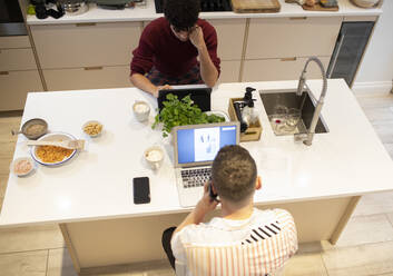 Junges schwules männliches Paar arbeitet von zu Hause aus an Laptops in der Küche - CAIF31116