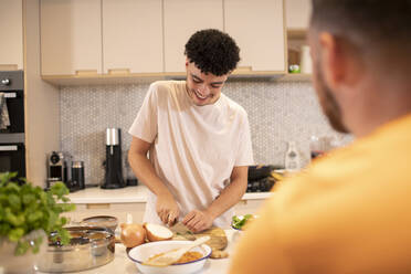 Junger Mann beim Kochen und Schneiden von Zwiebeln in der Küche - CAIF31122