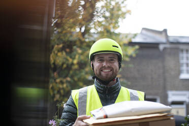 Portrait friendly delivery man in helmet delivering packages at door - CAIF31128