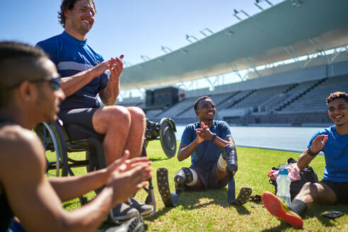 Paraplegic and amputee male athletes clapping on sunny stadium grass - CAIF31144