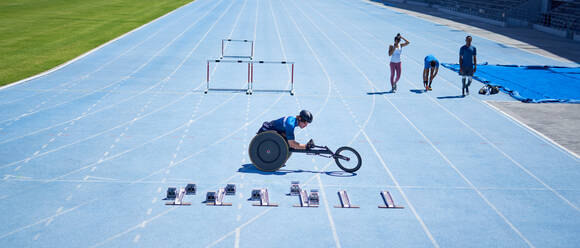Wheelchair athlete preparing on sunny blue sports track - CAIF31150