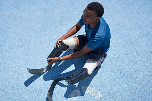 Male amputee sprinter preparing on blue sports track - CAIF31153