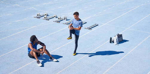 Young male runners on sunny blue sports track - CAIF31155