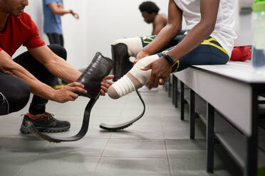 Coach helping male amputee athlete with running blade prosthetics - CAIF31177
