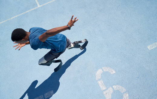 Male amputee athlete running on sunny blue sports track - CAIF31178