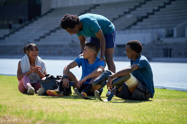 Happy athlete friends resting and talking on sunny stadium grass - CAIF31182