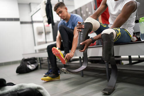 Male amputee athlete adjusting running blade prosthetic in locker room - CAIF31199