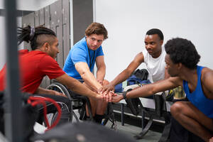 Amputee and wheelchair athletes joining hands in huddle in locker room - CAIF31211