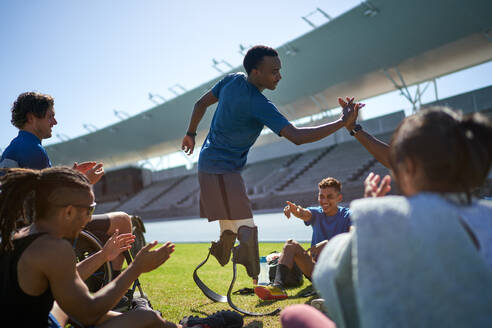 Happy male amputee athlete high fiving with friend in stadium - CAIF31219