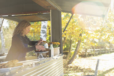 Die Besitzerin eines Imbisswagens arrangiert Gebäck im sonnigen Herbstpark - CAIF31222