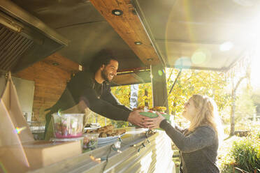 Glücklicher Foodtruck-Besitzer serviert Kunden im sonnigen Park Essen - CAIF31226