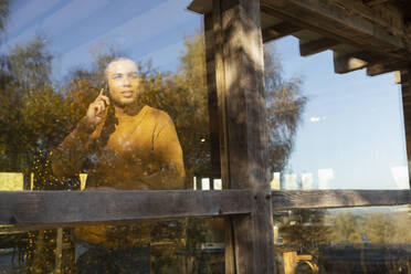 Man talking on smart phone at sunny restaurant window - CAIF31228