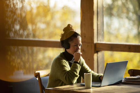 Geschäftsfrau mit Kopfhörern bei der Arbeit am Laptop in einem Café - CAIF31244