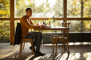 Geschäftsmann mit Papierkram bei der Arbeit in einem sonnigen Herbstcafé - CAIF31264