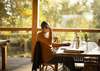 Businessman with headphones working at laptop in sunny autumn cafe - CAIF31307