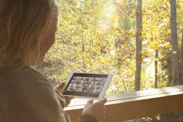 Frau im Videochat mit Freunden auf digitalem Tablet am Herbstfenster - CAIF31315