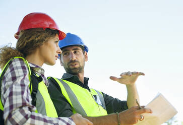 Male engineer gesturing while looking at female colleague - AJOF01508