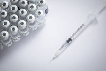 Close-up of some vials with the coronavirus vaccine along with a needle on a white background - ADSF25478
