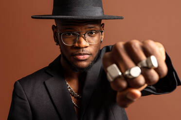 Young masculine unshaven African American male with naked abdomen in jacket looking at camera on brown background - ADSF25535