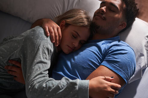 Von oben der heiteren multiethnischen Paar auf dem Bett liegen und umarmen, während in gemütlichen Schlafzimmer schlafen - ADSF25545