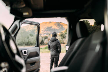 Rückansicht durch das Innere eines Autos eines Mannes, der die Berglandschaft bei Sonnenaufgang betrachtet - ADSF25557