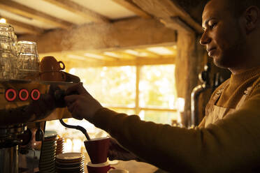 Männlicher Barista bereitet Cappuccino an einer Espressomaschine in einem Café zu - CAIF31324