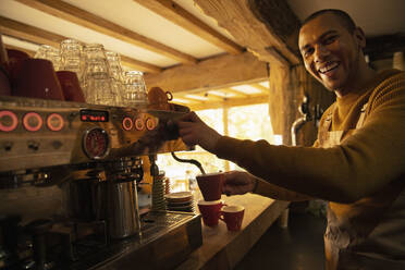 Porträt glücklicher männlicher Barista, der in einem Café an einer Espressomaschine Kaffee zubereitet - CAIF31331