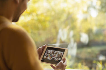 Mann führt Videochat mit Freunden auf einem digitalen Tablet-Bildschirm am Fenster - CAIF31351