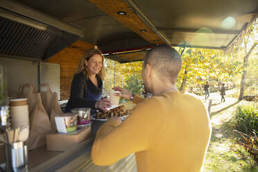 Friendly food cart owner serving coffee to customer in autumn park - CAIF31362