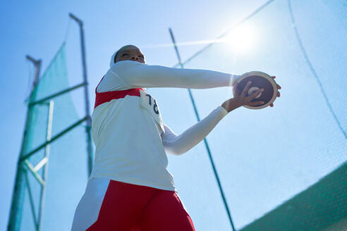 Leichtathletin beim Diskuswurf unter sonnigem, blauem Himmel - CAIF31391