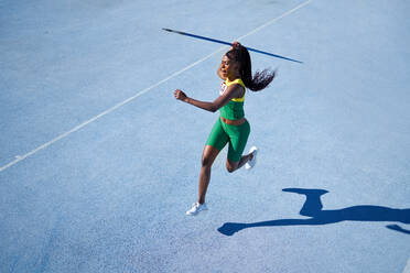 Female track and field athlete throwing javelin on sunny blue track - CAIF31412