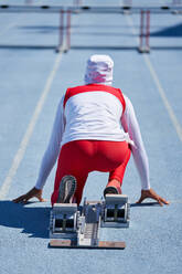 Female track and field athlete in hijab at starting block on track - CAIF31433