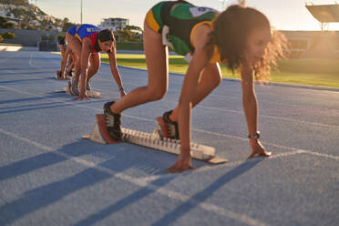 Female track and field athletes at starting blocks on sunny track - CAIF31436