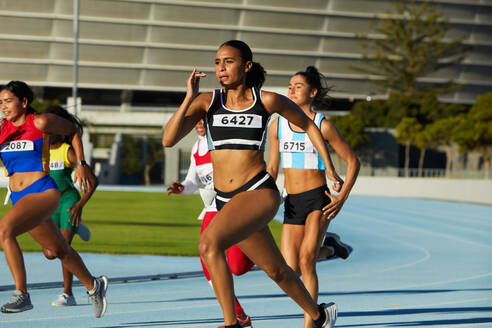 Female track and field athletes running in competition on race track - CAIF31442