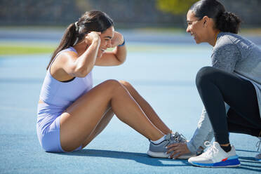 Happy female track and field athletes doing sit ups on track - CAIF31450